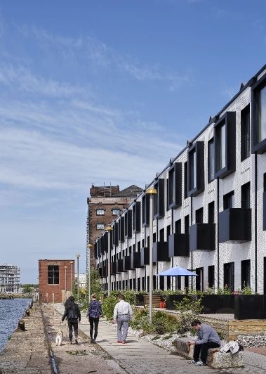 row of grey buildings next to the quay with people walking down he path in between.